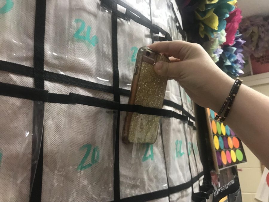 Student puts phone away in the phone caddy. The new phone policy began this year in order to improve grades and lower distractions in the classroom. 